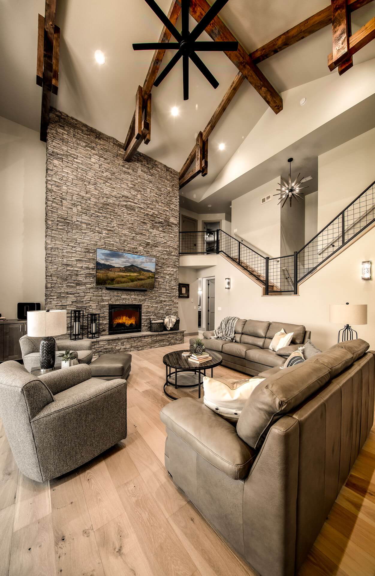 Two-story family room in Woodland Park Custom Home has beamed ceilings, a floor to ceiling fire place, and wood floors.